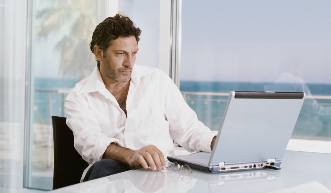גבר בחולצה לבנה יושב מול מחשב נייד על רקע ים